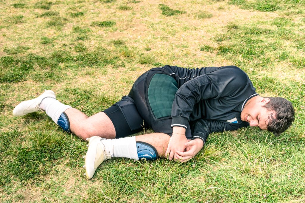 Fußballer nach einer Verletzung, liegt am Boden und hält sein schmerzendes Knie